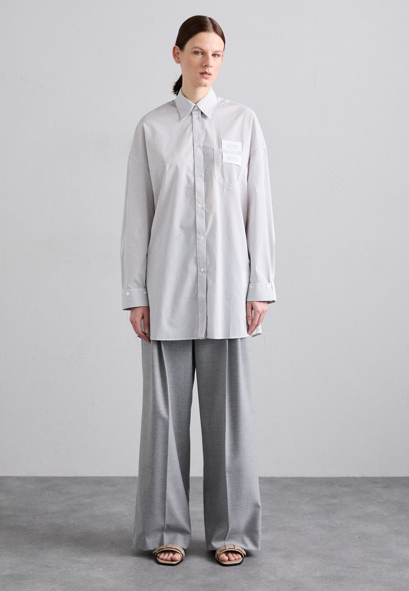 Chemise à rayures en tons clairs, coupe oversize avec une poche poitrine. Associée à un pantalon gris ample et des sandales plates. Design minimal.