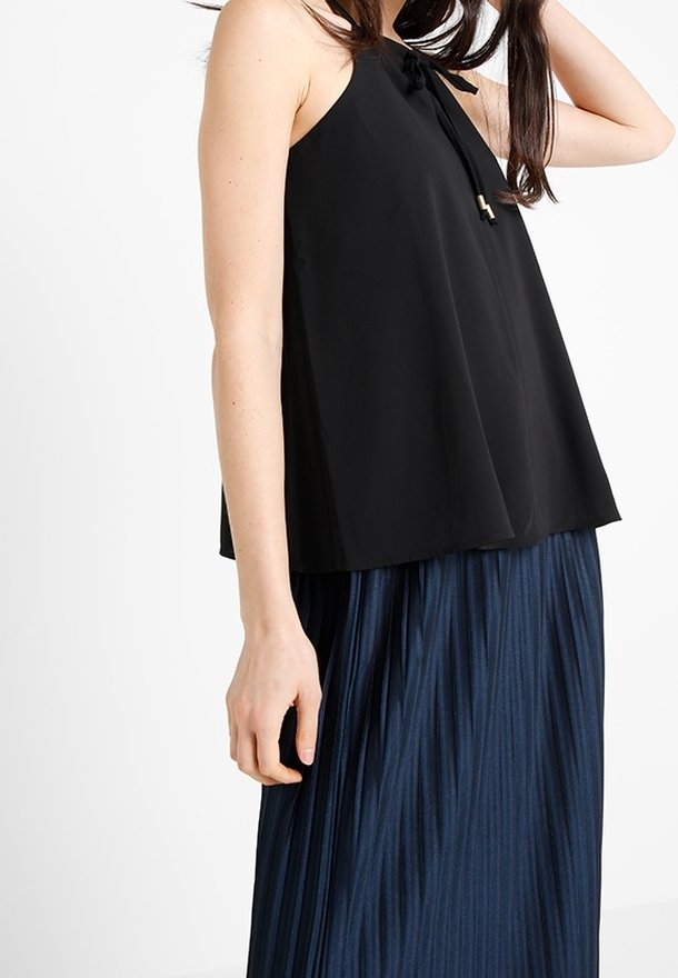 Svart ärmlös topp med en knytning vid halsringningen och en lös, flytande design, i kombination med en plisserad marinblå kjol.