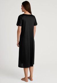 Abito nero di lunghezza al ginocchio realizzato in tessuto morbido, con maniche corte e scollatura rotonda, progettato con una vestibilità ampia e rilassata.