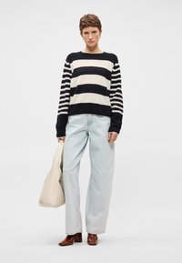 Sweater às riscas em azul marinho e creme, com mangas longas e caimento solto. Jeans de perna larga em azul claro e mules de salto castanho. Bolsa tote creme.
