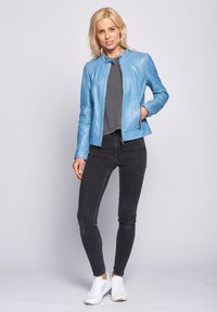 Ljusblå skinnjacka med ståkrage, dragkedja och två sidofickor, tillsammans med svarta skinny jeans och vita sneakers.