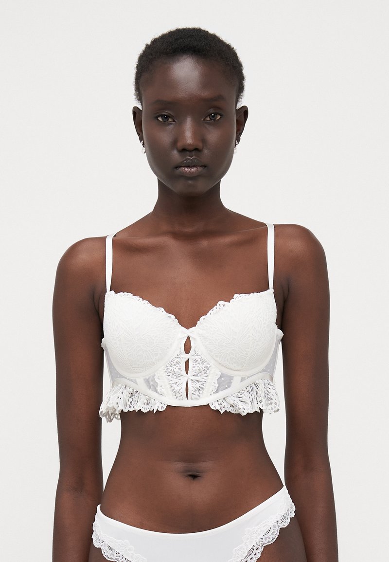 Hvit blondet bralette med en strukturert design, bølgete kanter og dekorative frontkutte. Justerbare skulderstropper inkludert.