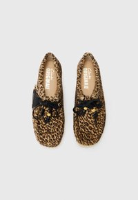 Lepardmønstrede slippers lavet af blødt materiale, med en rund form, sorte snørebånd med træperler og en polstret sål.