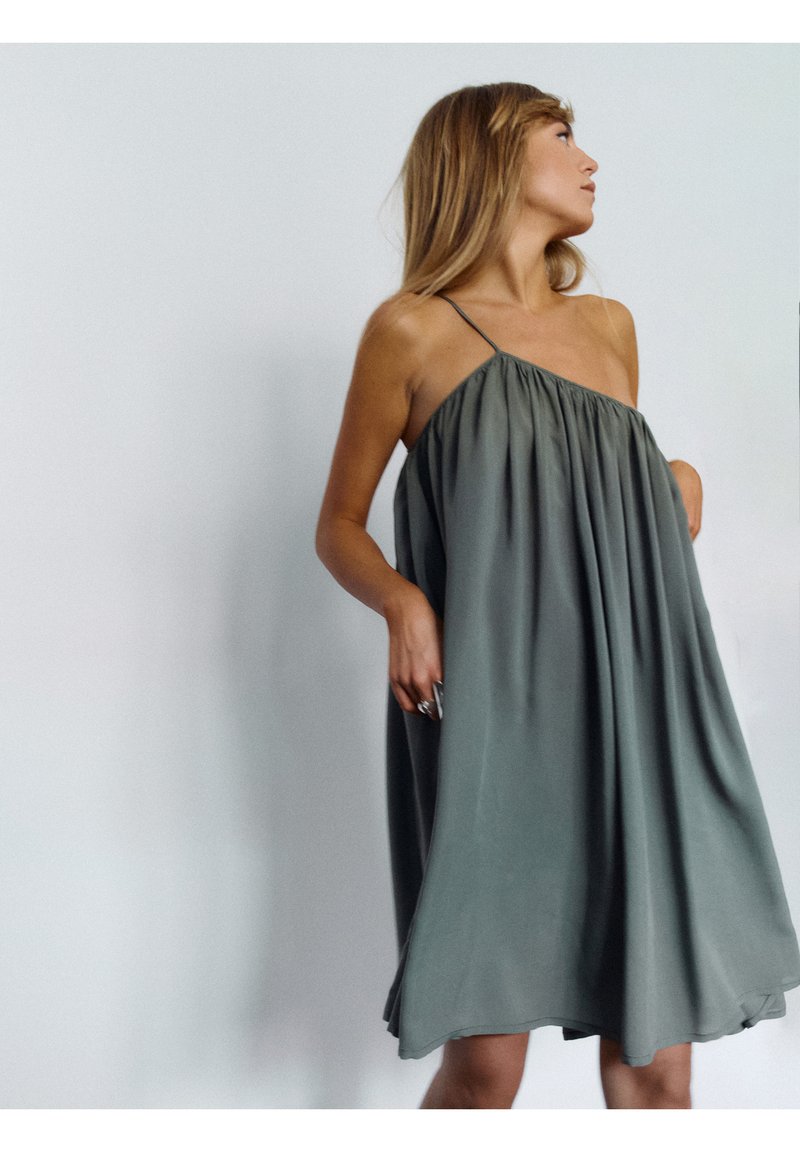 Jasnozielona, bezrękawnikowa sukienka z luźnym, marszczonym topem i cienkimi ramiączkami. Gładki materiał opada do długości kolan.