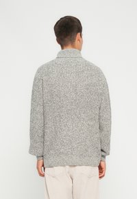 Maglione grigio lavorato a maglia con colletto alto, caratterizzato da un motivo testurizzato e maniche ampie, mostrato da dietro.