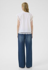 Top de algodón blanco con dobladillo festoneado y mangas rizadas, combinado con unos jeans de denim azul medio de corte holgado y terminación deslavada.