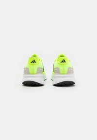 Zapatillas deportivas en color amarillo fluorescente con parte superior sintética, entresuela blanca y suela exterior de goma negra. La vista trasera muestra acentos de logotipo.