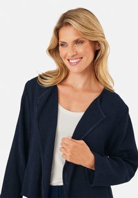 Marineblaues strukturiertes Jacket mit entspannter Passform, offenem Frontbereich und langen Ärmeln. Verfügt über einen kontrastierenden Besatz am Kragen für zusätzliche Details.