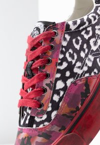 Basket avec une tige en tissu à motifs mettant en avant un imprimé léopard rose, noir et blanc, des lacets rouges et des œillets métalliques ; semelle en caoutchouc.