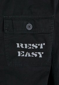 Črni tkaninski žep z gumbom, s frazo "REST EASY" natisnjeno v krepkem, stiliziranem sivo besedilu.