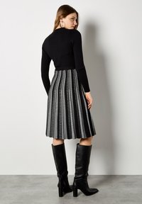 Czarny wydłużony top z prążkami z długim rękawem w zestawieniu z plisowaną spódnicą w pionowe czarno-białe paski. Czarne kozaki na obcasie do kolan.