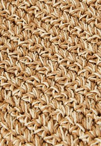 Wykonana z naturalnych włókien, pleciona dywanik w kolorze tan i kremowym, z teksturowaną powierzchnią oraz skomplikowanym przeplatanym wzorem.