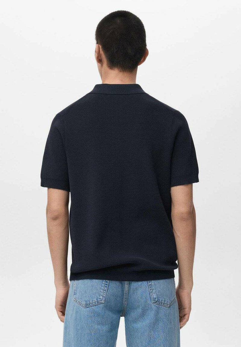 Marineblaues Poloshirt mit kurzen Ärmeln aus strukturiertem Strick, mit Kragen. Getragen zu hellblauen Jeans, Rückansicht gezeigt.