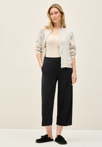 Lichtgrijs bomberjack over een beige top, gecombineerd met zwarte cropped pants en zwarte instappers. Soepele texturen en een relaxte pasvorm.