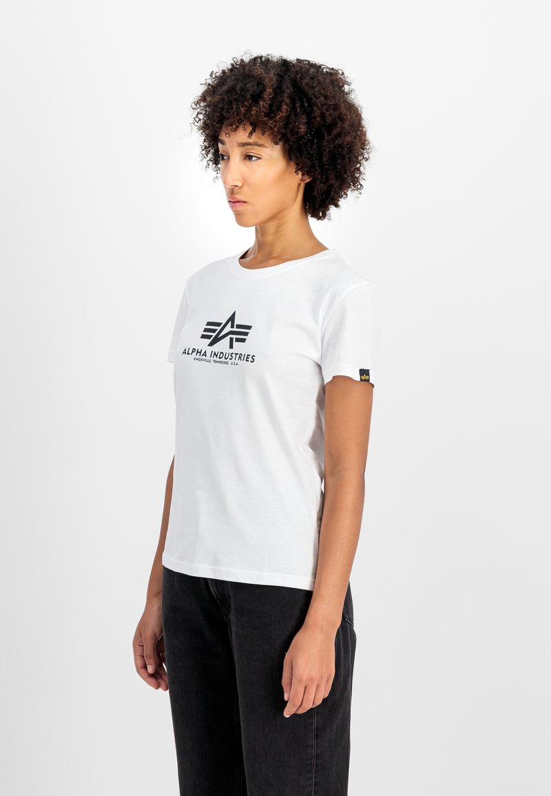 Bijela pamučna majica s crnim grafičkim logom na prsima i malom žutom etiketom na rukavu. Kratki rukavi i okrugli izrez.