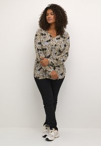 Long-sleeve, collared blouse in beige with blue and black floral print. Paired with black pants and light-colored sneakers.