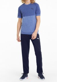 Blue athletic t-shirt with textured upper section and solid lower section, paired with navy pants. Both items feature a subtle logo.