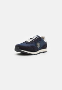 Črne nubuk in denim tenisice z belimi vezalkami, okroglo značko in teksturirano gumijasto podplato z rahlim peto.
