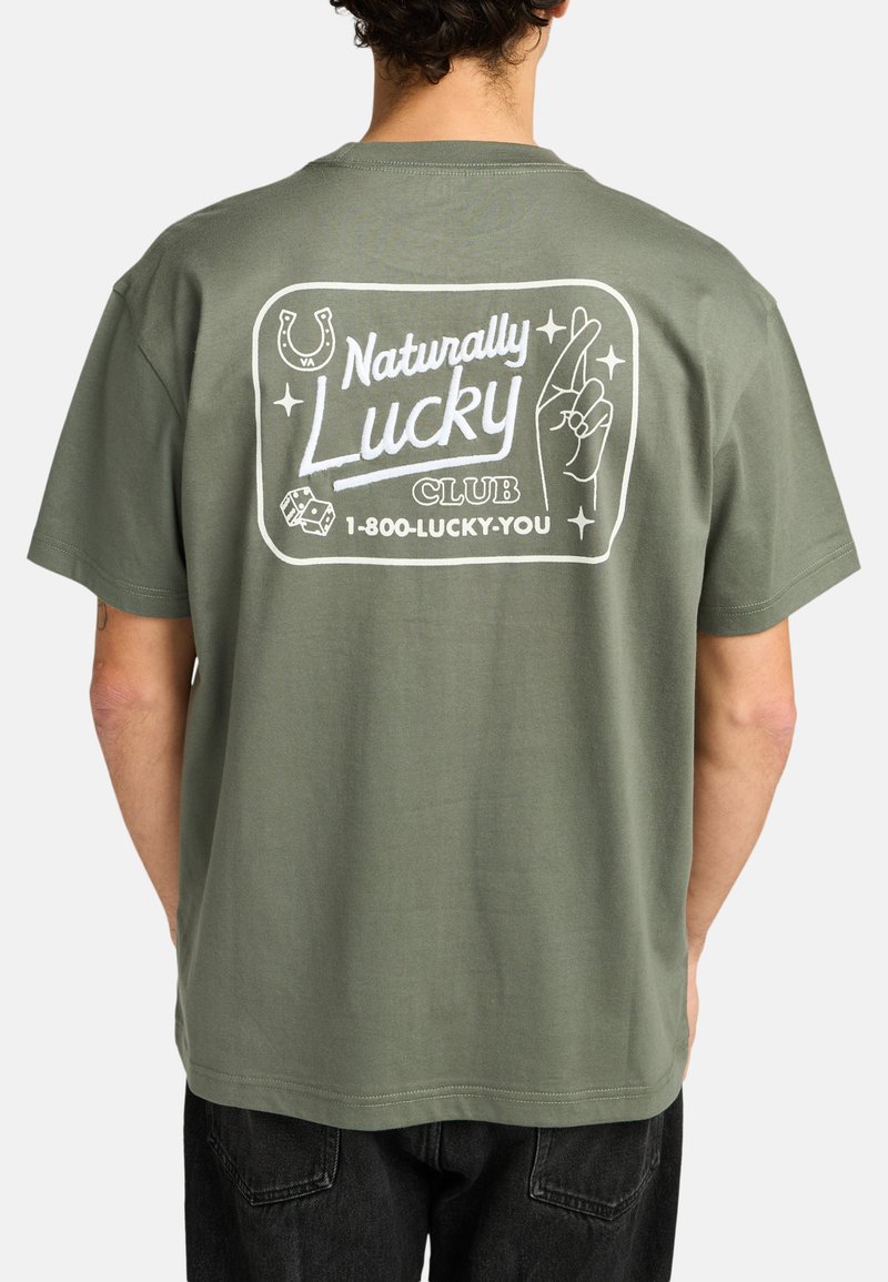 Camiseta de algodón verde con un diseño gráfico en la parte posterior que incluye el texto "Naturally Lucky Club" y ilustraciones de un herradura, una mano y dados.