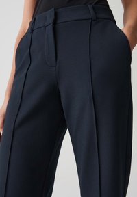 Navyblauwe op maat gemaakte broek van soepel stof, met een vlakke voorkant, twee zijzakken en subtiele plooidetails langs de benen.