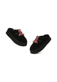 Black suede clogs with a textured sole, featuring a colorful woven tassel detail at the front and a soft, plush interior lining.