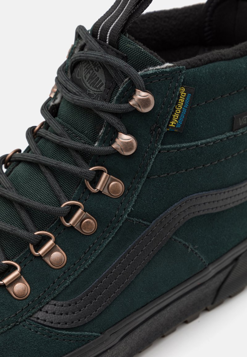 Ciemnozielone wysokie trampki wykonane z zamszu i tekstyliów, z miedzianymi przelotkami, czarnymi akcentami i teksturowaną gumową podeszwą. Zawierają etykietę HydroGuard.