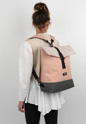 Zaino rosa e grigio con design a risvolto, realizzato in tessuto. Dotato di accessori neri e spallacci regolabili, presentato su un modello.