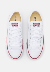 Paire de baskets basses blanches Converse All Star avec une bordure rouge et des lacets blancs, vue de dessus sur fond blanc.