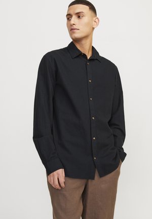 Lange mouwen zwarte blouse gemaakt van een lichte stof met een kraag en houten knopen, gecombineerd met lichtbruine broeken.