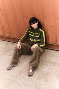 Green zip-up jacket with yellow and white stripes, corduroy tan wide-leg pants, and brown slip-on shoes with straps. Flat surface background.