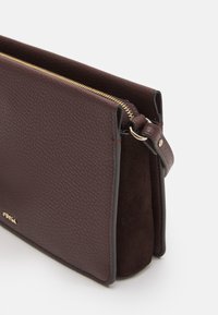 Burgundowa skórzana torba na zamek błyskawiczny z teksturowaną powierzchnią i zamszowymi akcentami. Posiada boczny pasek i złote wykończenie zamka.