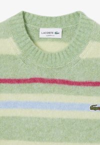 Maglione a righe verde e crema con bande rosse e blu; caratteristiche di un collo a girocoscia a costine; logo Lacoste sul lato sinistro. Texture a maglia morbida.