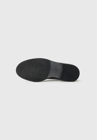 Semelle de chaussure noire avec une texture lisse, de forme légèrement arrondie, présentant un subtil détail de logo en relief près du talon.