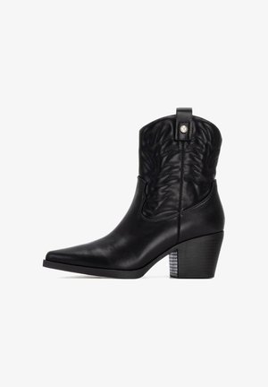 Botas de cowboy de cuero negro con punta afilada, patrón floral en relieve en la caña y un tacón grueso y a rayas. Presenta una lengüeta para facilitar su puesta.