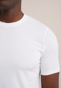 Camiseta blanca de algodón de manga corta con cuello redondo. Textura suave y diseño ajustado, con costuras sutiles a lo largo del cuello y las mangas.