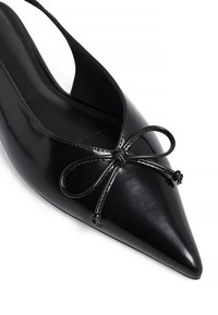Pompe en cuir verni noir à bout pointu, avec un accent de nœud décoratif, un devant dégagé et un design de bride arrière.