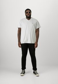 Tricou gri cu decolteu în V, pantaloni negri slim-fit și adidași negri cu glezna înaltă. Accesoriile includ ochelari rotunzi de soare. Textură netedă, design casual.