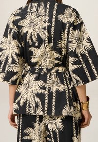 Kimono di stoffa nera con motivo di foglie di palma color crema. Presenta maniche ampie, una vita cintrata e una vestibilità comoda. Texture liscia, design leggero.