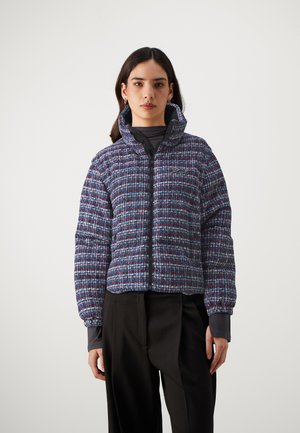 Gewatteerde jas in blauw, rood en wit geweven stof. Heeft een hoge kraag, ritssluiting en elastische manchetten. Korte ontwerp met textuurpatroon.