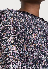 Top in tessuto nero con motivo floreale multicolore. Presenta dettagli arricciati e scollatura a forma di conchiglia. Texture morbida con vestibilità comoda.
