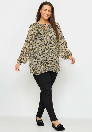Beige paita, jossa on musta leopardikuvio, pitkät hihat ja avainaukko-kaula-aukko, yhdistetty mustiin slim-fit-housuihin ja mustiin loafereihin.
