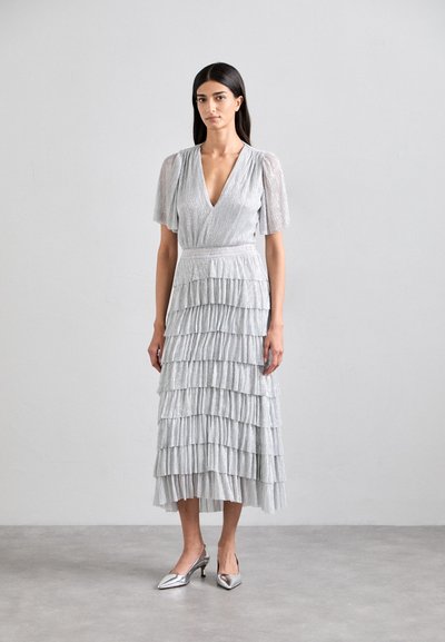 Silver, tiered dress with a deep V-neck and short puff sleeves. Made of a textured, shimmery fabric. Paired with metallic, pointed-toe heels.