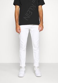 Valkoiset slim fit -farkut, puuvillamateriaalia, edessä taskut ja käännetty helma, yhdistetty mustaan t-paitaan ja valkoisiin tennareihin.