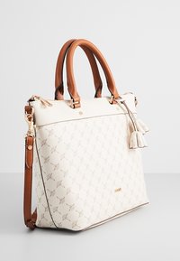 Sac à main crème avec anses et bandoulière marron, motif géométrique embossé, quincaillerie dorée et pampilles décoratives sur fond uni.