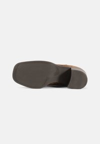 Talpa de pantof din suede maro cu o suprafață texturată de cauciuc, având striuri orizontale și o formă curbată la călcâi.
