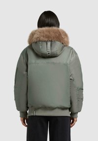 Padded jacket w kolorze oliwkowym z kołnierzem z sztucznego futra. Posiada kaptur, ściągacze przy mankietach oraz pudełkowy krój, eksponując gładką fakturę.