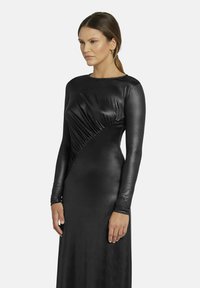 Schwarzes Langarmkleid mit tailliertem Schnitt, glatter satinähnlicher Textur und horizontalen Raffungselementen auf der linken Seite.