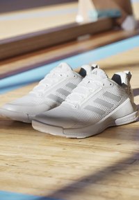 White athletic shoes featuring a textured upper, three gray stripes, laces, and a rubber outsole. Accented with a logo on the tongue.