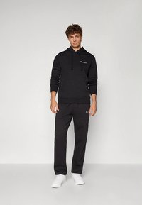 Felpa nera con cappuccio, tasca frontale e coulisse, abbinata a pantaloni della tuta neri coordinati; entrambi con piccolo logo sul petto e sulla coscia.