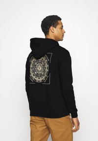 Black hoodie featuring a large gold graphic design on the back, with a textured pattern and a drawstring hood. Casual fit.